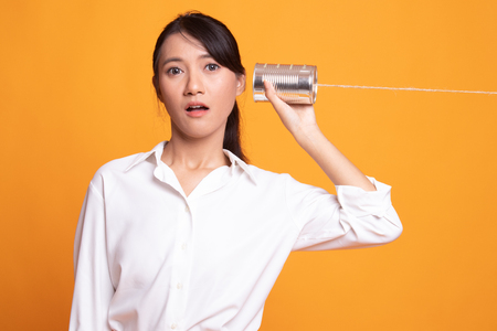 Surprised young Asian woman with tin can phone on yellow backgroundの写真素材