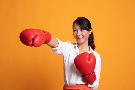 Young Asian woman with red boxing gloves on yellow backgroundの写真素材