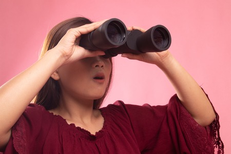 Young Asian woman with binoculars on pink backgroundの写真素材