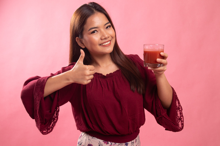 Young Asian woman thumbs up with tomato juice on pink backgroundの写真素材