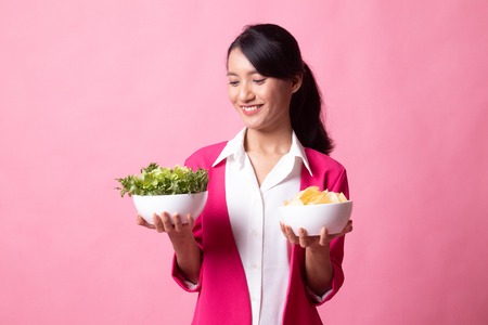 Young Asian woman with potato chips and salad on pink backgroundの写真素材