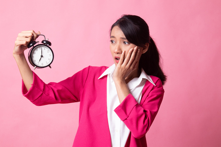 Young Asian woman is stressed with a clock on pink backgroundの写真素材