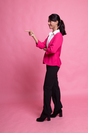Full body side view of beautiful young asian woman pointing on pink backgroundの写真素材