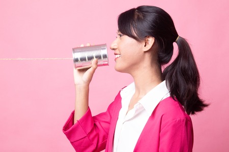 Young Asian woman with tin can phone on pink backgroundの写真素材