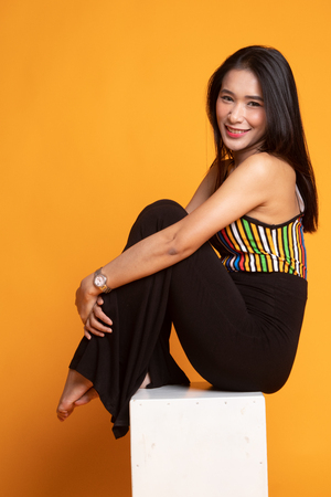 Portrait of beautiful young Asian woman in colorful shirt is sitting on yellow backgroundの写真素材