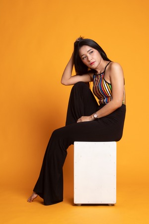 Portrait of beautiful young Asian woman in colorful shirt is sitting on yellow backgroundの写真素材