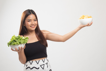 Young Asian woman with potato chips and salad on white backgroundの写真素材