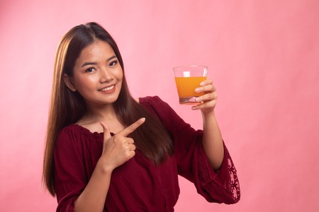Young Asian woman point to orange juice on pink backgroundの写真素材