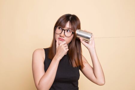 Young Asian woman hearing with tin can phone and thinking  on beige backgroundの写真素材