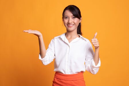 Beautiful young Asian woman show palm hand and thumbs up on yellow backgroundの写真素材