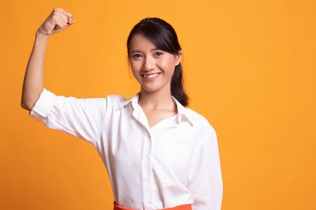 Beautiful young Asian woman flex bicep on yellow backgroundの写真素材