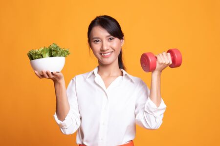 Healthy Asian woman with dumbbells and salad on yellow backgroundの写真素材