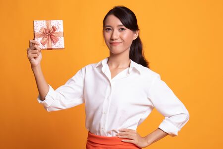 Young Asian woman with a gift box on yellow backgroundの写真素材