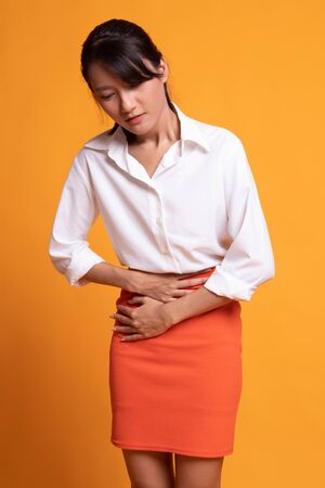 Young Asian woman got stomachache on yellow backgroundの写真素材