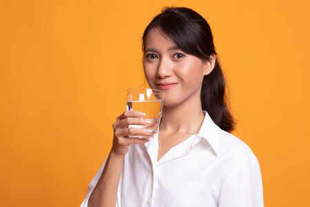 Young Asian woman with a glass of drinking water on yellow background