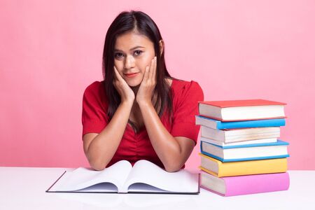 Young Asian woman read a book with books on table on pink backgroundの写真素材