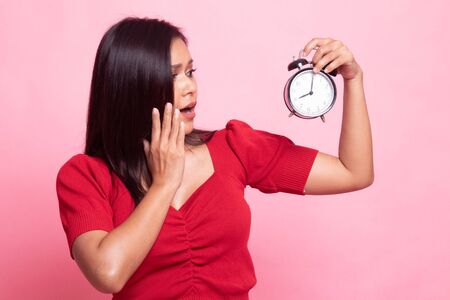 Young Asian woman is stressed with a clock on pink backgroundの写真素材