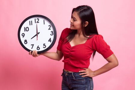 Young Asian woman with a clock on pink backgroundの写真素材