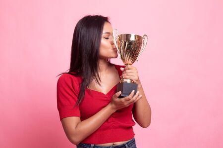 Successful young asian woman holding kissing a trophy on pink backgroundの写真素材