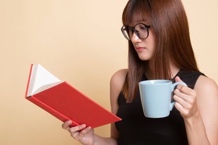 Young Asian woman with a book and cup of coffee  on beige background