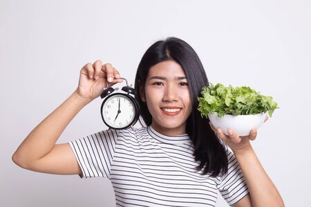 Young Asian woman with clock and salad on white backgroundの写真素材