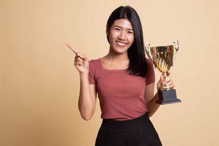 Successful young asian woman holding a trophy point to blank space on beige backgroundの写真素材