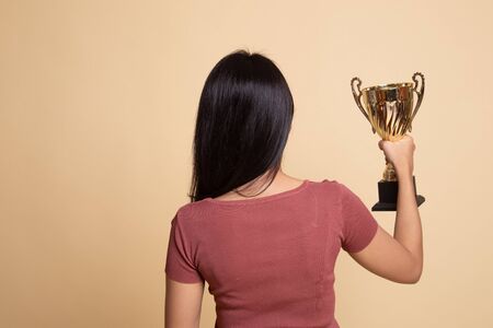 Back view of successful young asian woman holding a trophy on beige backgroundの写真素材
