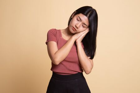 Beautiful young Asian woman with sleeping gesture on beige backgroundの写真素材