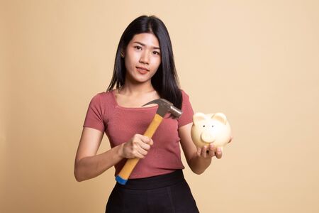 Asian woman with pig coin bank and hammer on beige backgroundの写真素材