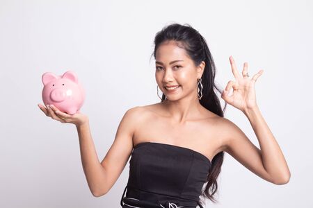 Asian woman show OK  with pig coin bank on white backgroundの写真素材
