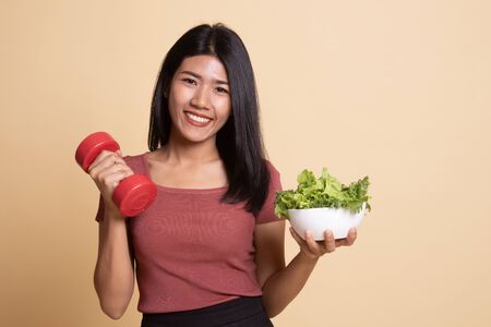 Healthy Asian woman with dumbbells and salad on beige backgroundの写真素材
