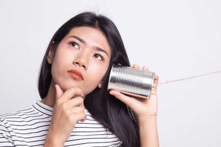 Young Asian woman hearing with tin can phone and thinking on white backgroundの写真素材