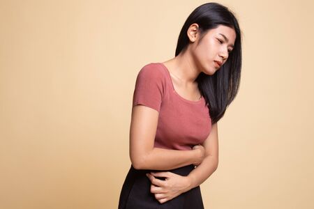 Young Asian woman got stomachache on beige backgroundの写真素材