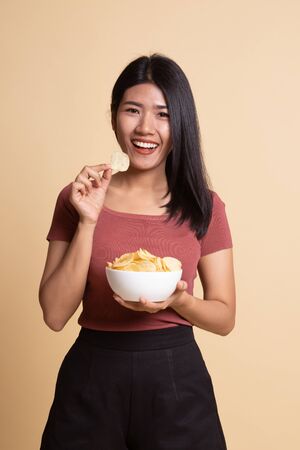 Young Asian woman eat potato chips on beige background