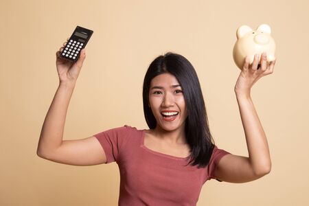 Asian woman with calculator and piggy bank on beige backgroundの写真素材
