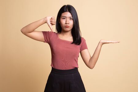 Young Asian woman show palm hand and thumbs down on beige background
