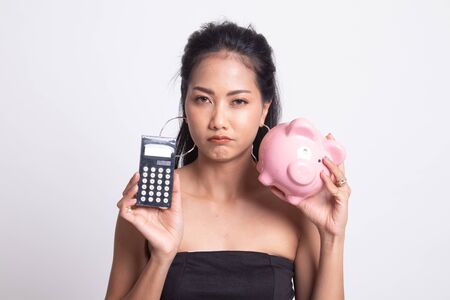 Unhappy Asian woman with calculator and piggy bank on white backgroundの写真素材