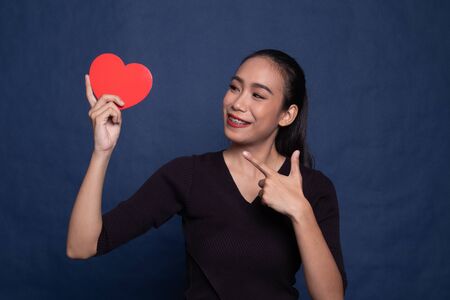 Asian woman point to red heart on blue background