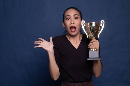 Successful young asian woman holding a trophy on blue backgroundの写真素材