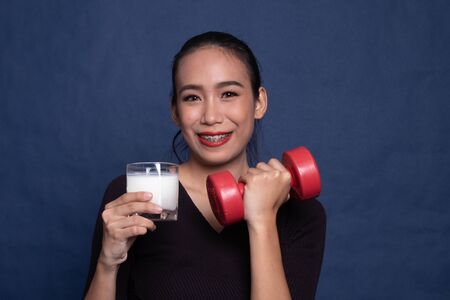 Healthy Asian woman drinking a glass of milk and dumbbell on blue backgroundの写真素材