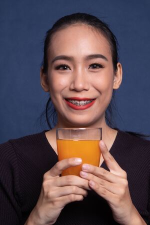 Young Asian woman drink orange juice on blue backgroundの写真素材