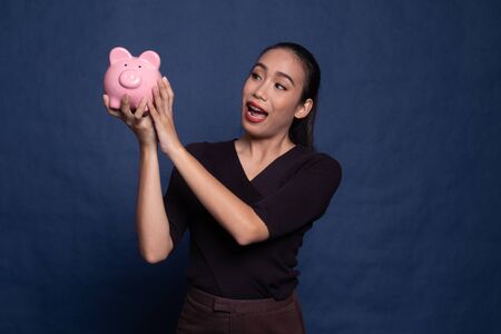 Young Asian woman kiss  a pink coin bank on blue backgroundの写真素材