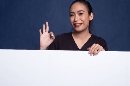 Young Asian woman show OK with blank sign on blue backgroundの写真素材