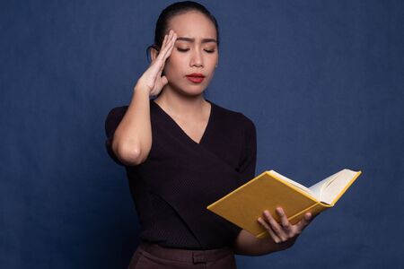 Young Asian woman got headache read a book on blue backgroundの写真素材