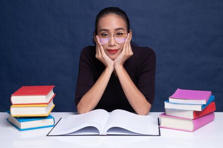 Young Asian woman read a book with books on table on blue background
