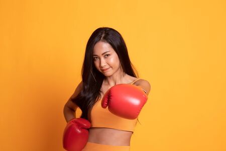 Young Asian woman with red boxing gloves on yellow backgroundの写真素材