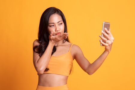 Young Asian woman with mobile phone on yellow backgroundの写真素材