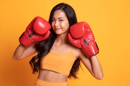 Young Asian woman with red boxing gloves on yellow backgroundの写真素材
