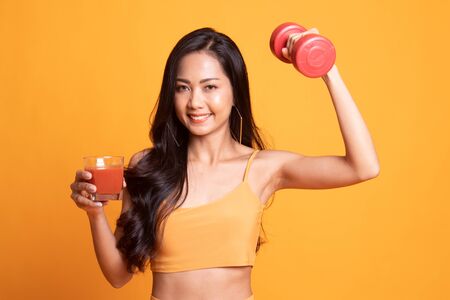 Young healthy Asian woman with dumbbell and  tomato juice on yellow backgroundの写真素材