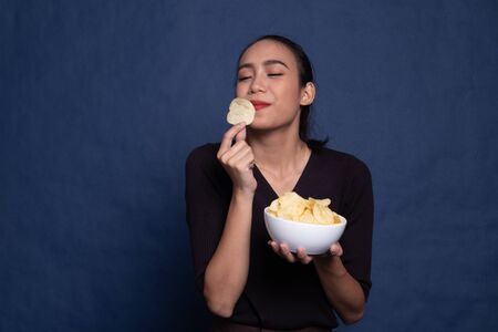 Young Asian woman eat potato chips on blue backgroundの写真素材